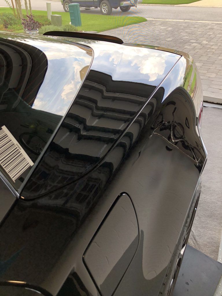 A black car is parked in a garage with the hood up.