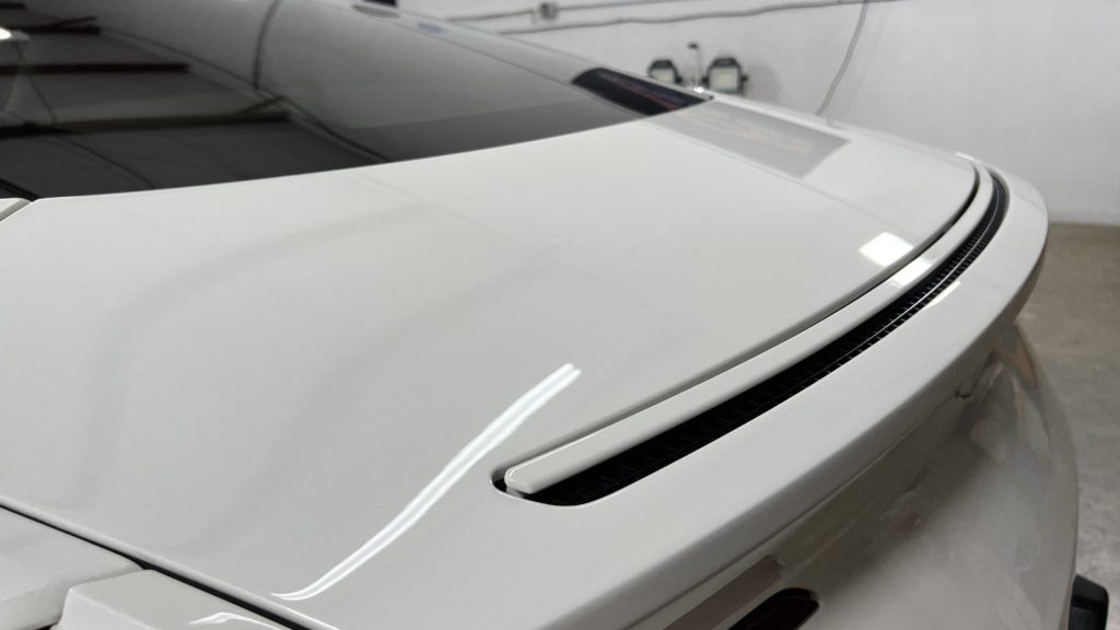 A white car with a black spoiler is parked in a garage.