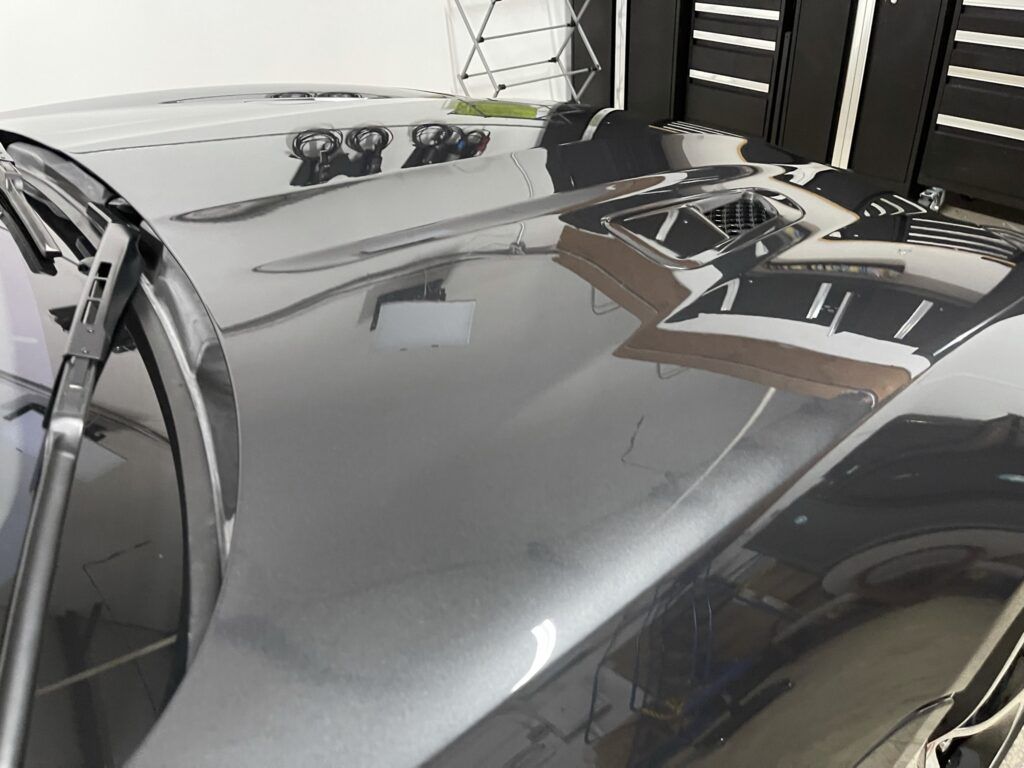 A close up of a car hood with a reflection of a building