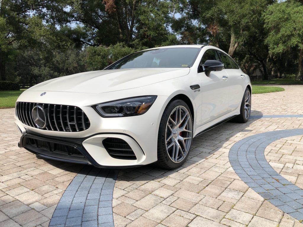 A white mercedes amg gt 63 s coupe is parked on a brick driveway.