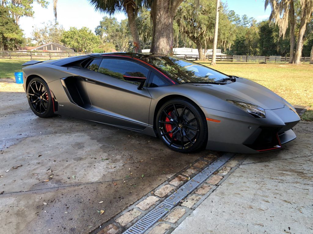 A gray lamborghini aventador is parked in a driveway.