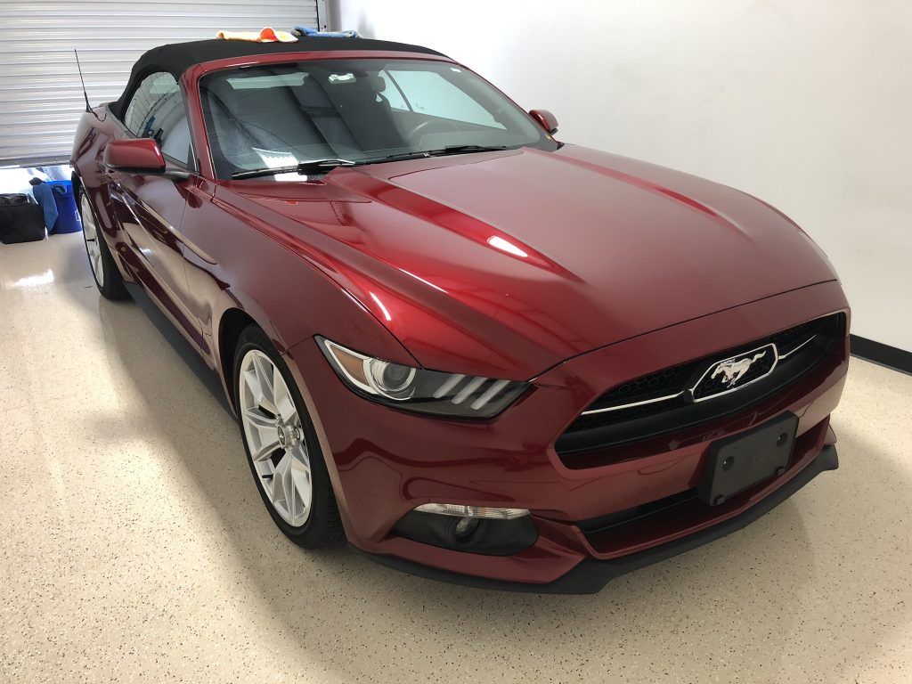 A red ford mustang convertible is parked in a garage.