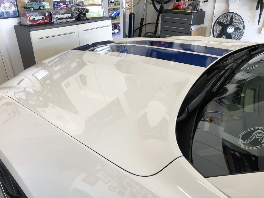 A white car is parked in a garage with a fan in the background.