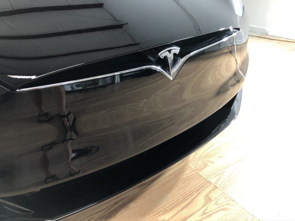 The front of a black tesla model s is sitting on a wooden floor.