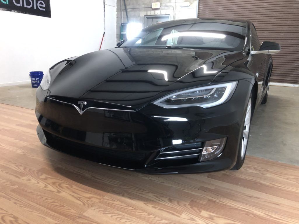A black tesla model s is parked on a wooden floor in a garage.