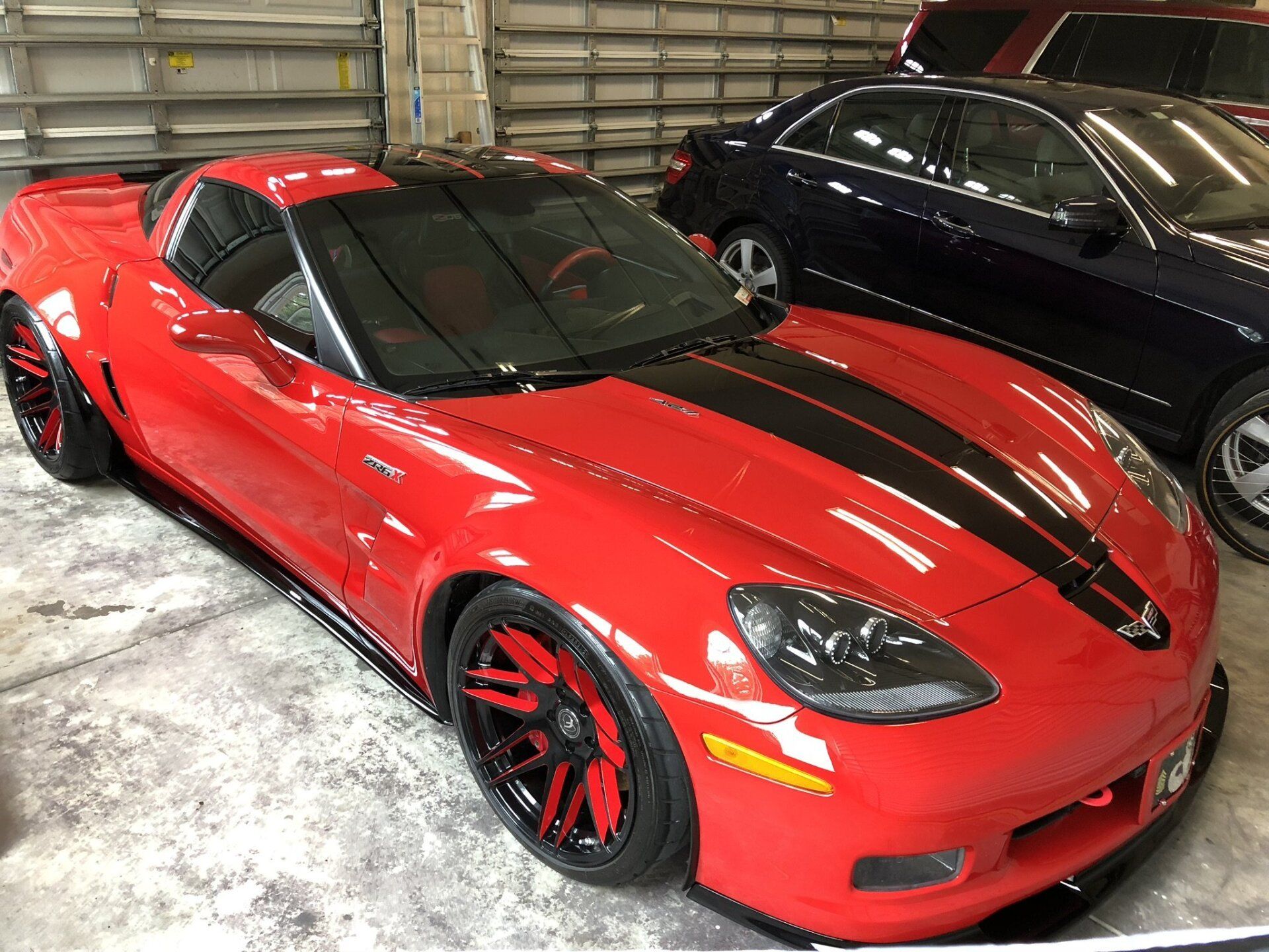 A red sports car with black stripes on the hood is parked in a garage.