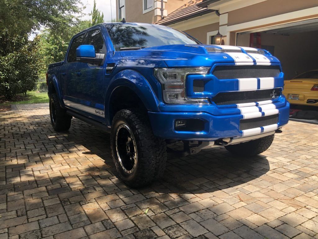 A blue truck is parked in a driveway next to a yellow car.