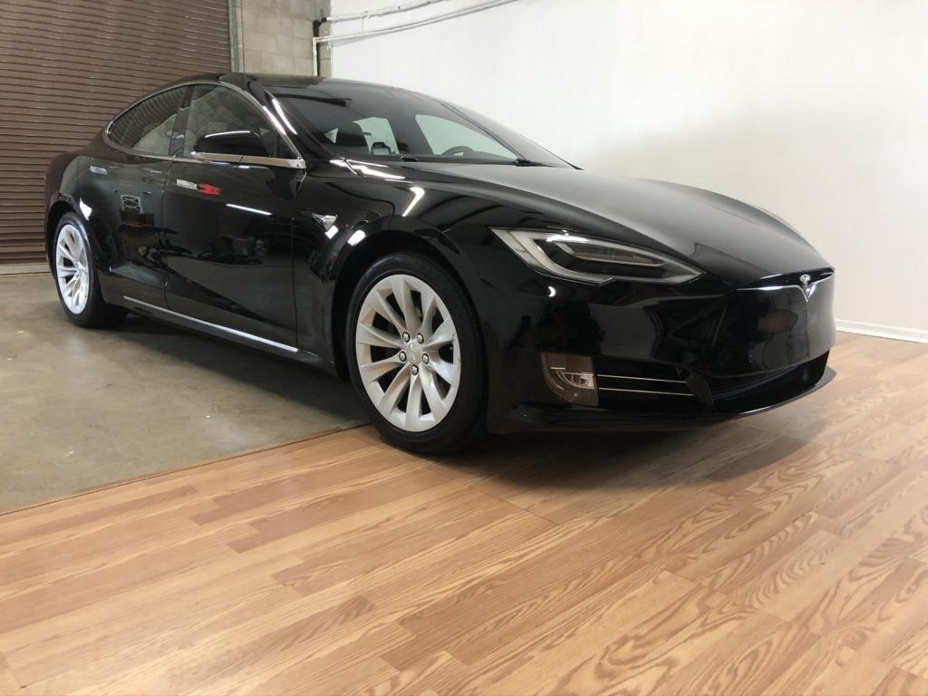 A black tesla model s is parked on a wooden floor in a garage.