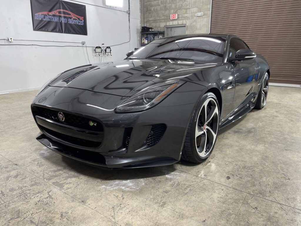 A black jaguar f type is parked in a garage.