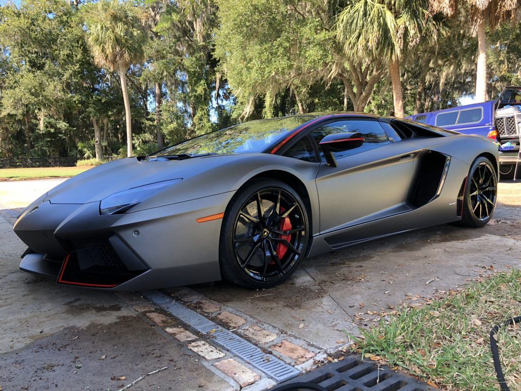 A gray lamborghini aventador is parked on the side of the road.