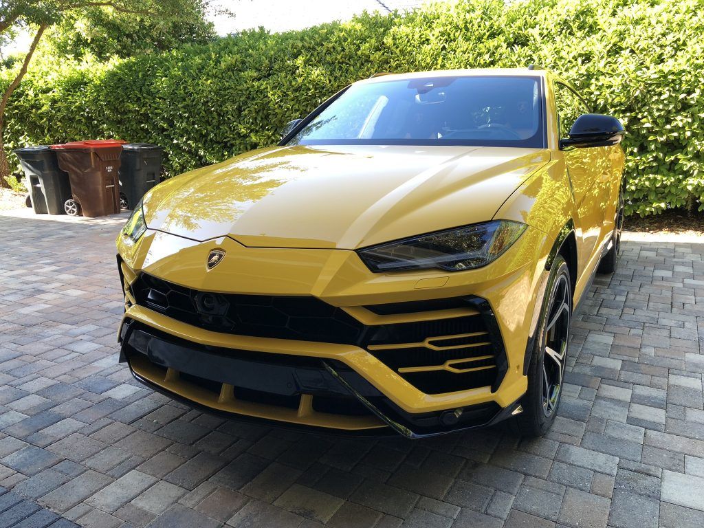 A yellow lamborghini urus is parked on a brick driveway.