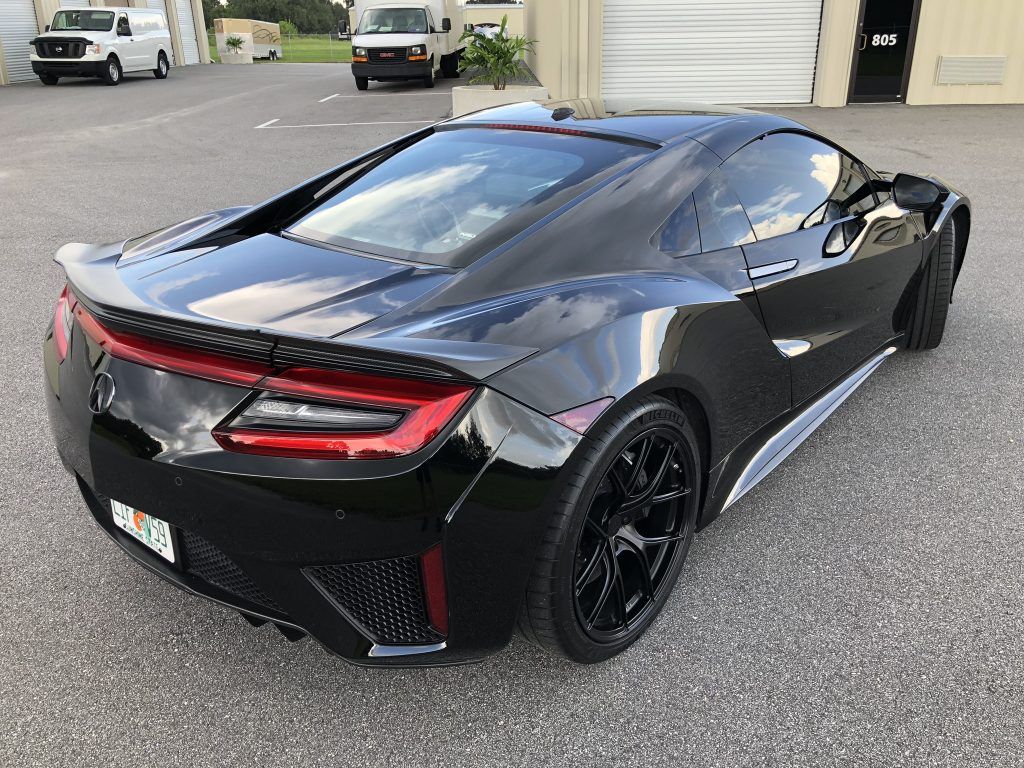 A black sports car is parked in a parking lot in front of a garage.