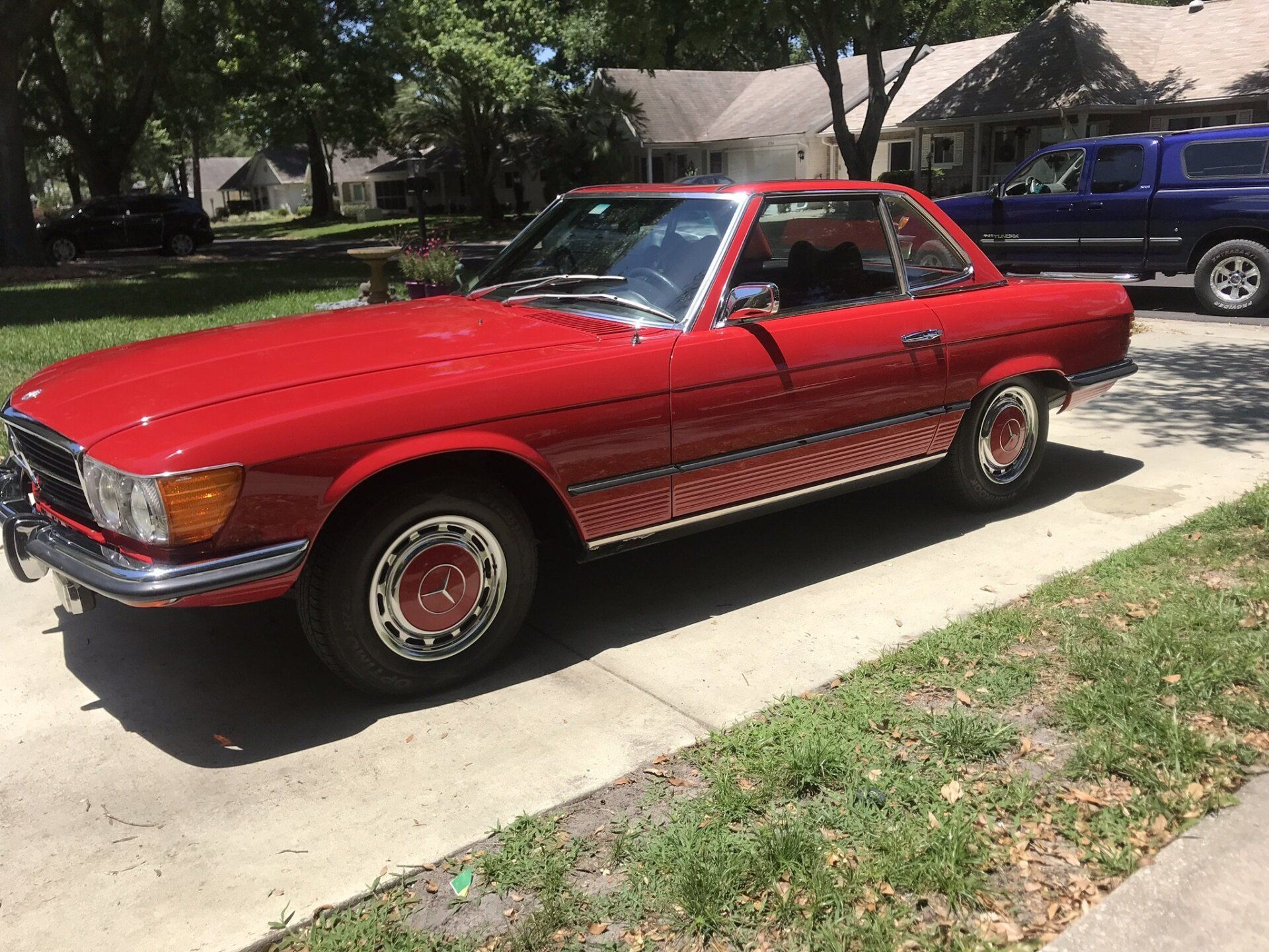 A red car is parked on the side of the road in front of a house.