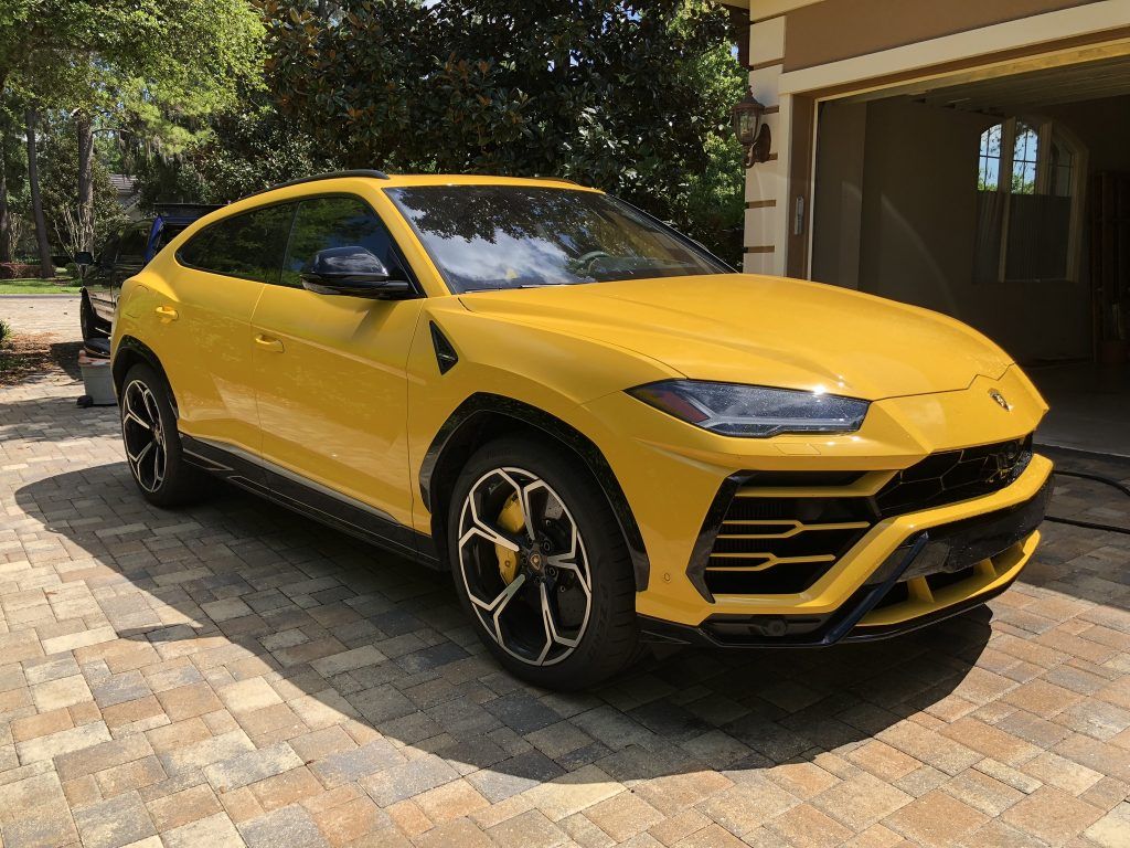 A yellow lamborghini urus is parked in front of a garage.