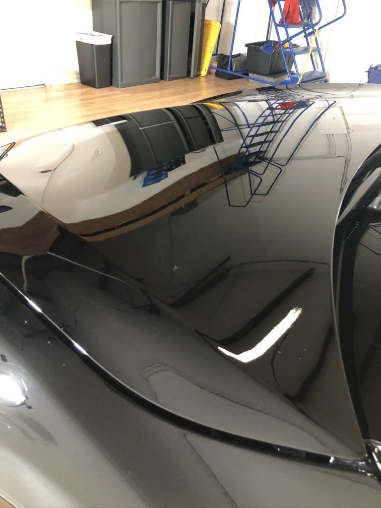 A black car is parked in a garage with a reflection of it in the hood.