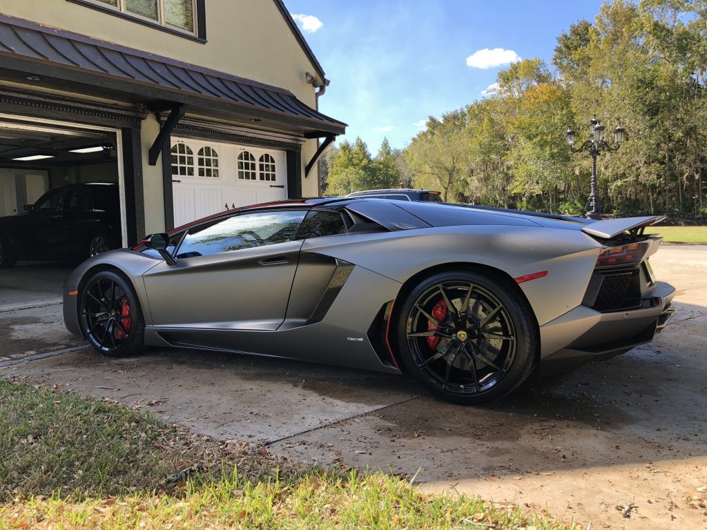 A silver lamborghini aventador is parked in front of a garage.