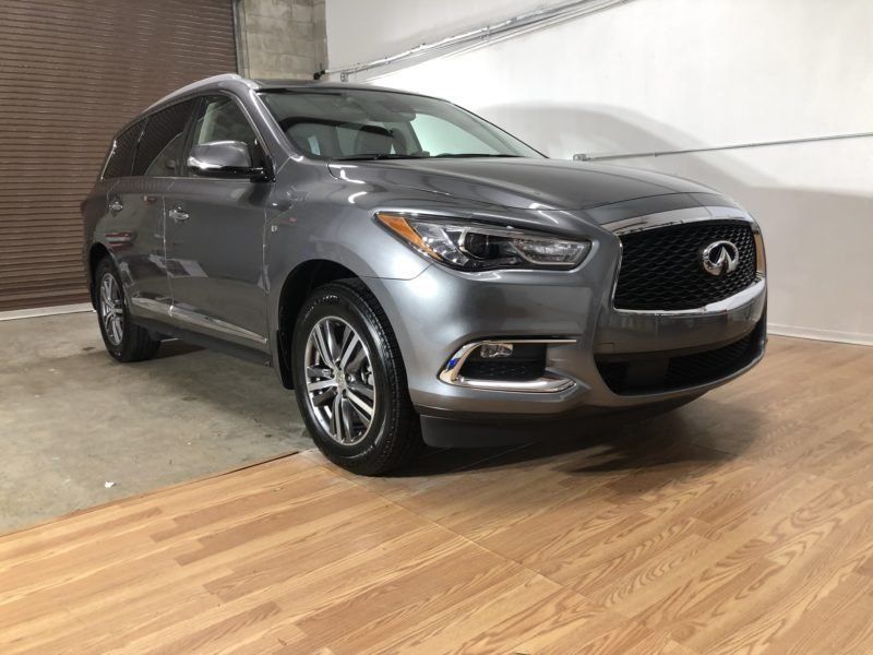 A silver infiniti q50 is parked on a wooden floor in a garage.