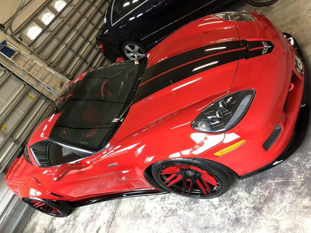A red sports car with black stripes is parked in a garage.