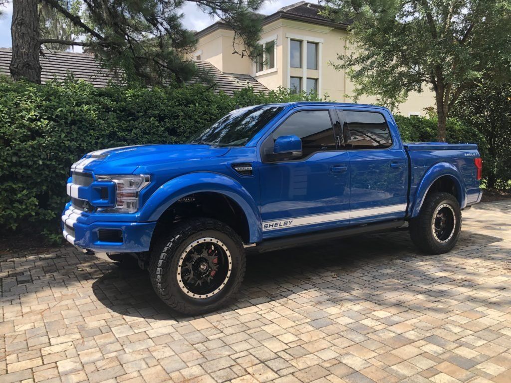 A blue pickup truck is parked on a brick driveway in front of a house.