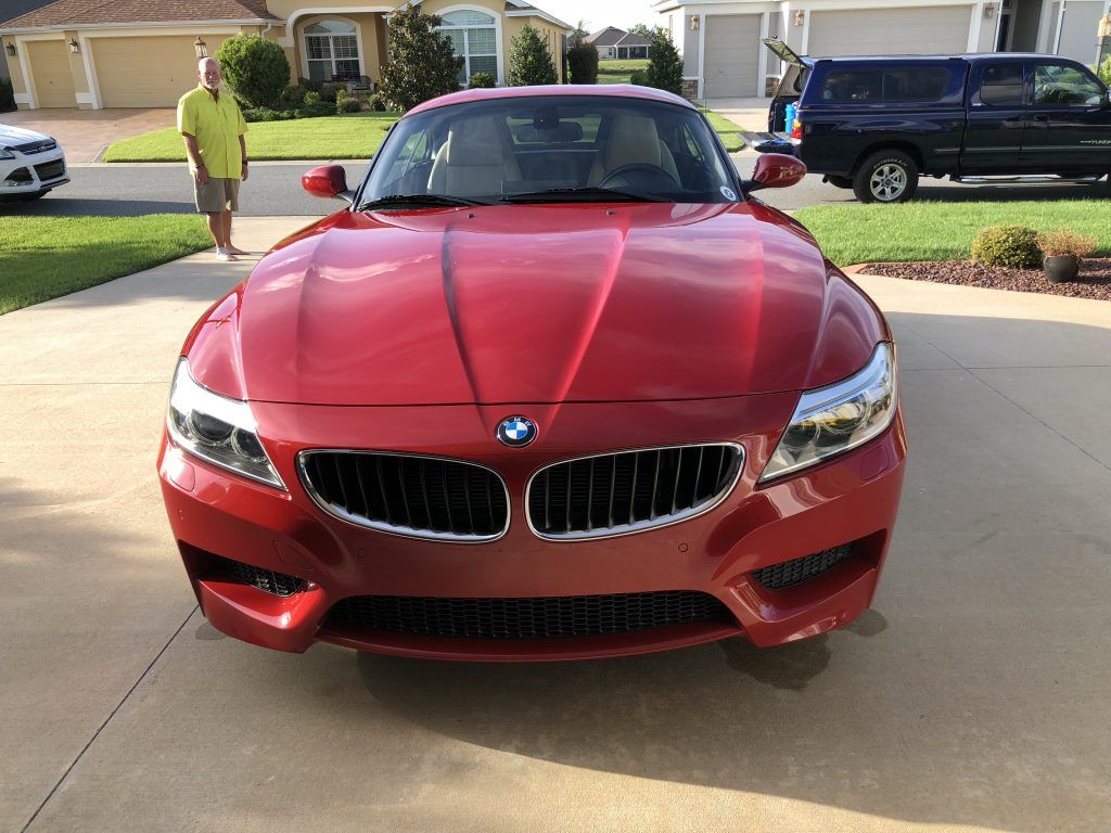 A red bmw z4 is parked in a driveway in front of a house.