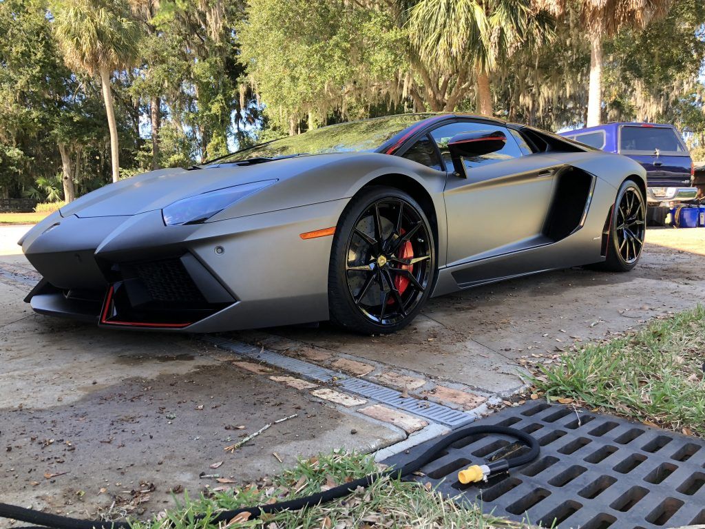 A lamborghini aventador is parked in a driveway next to a drain.