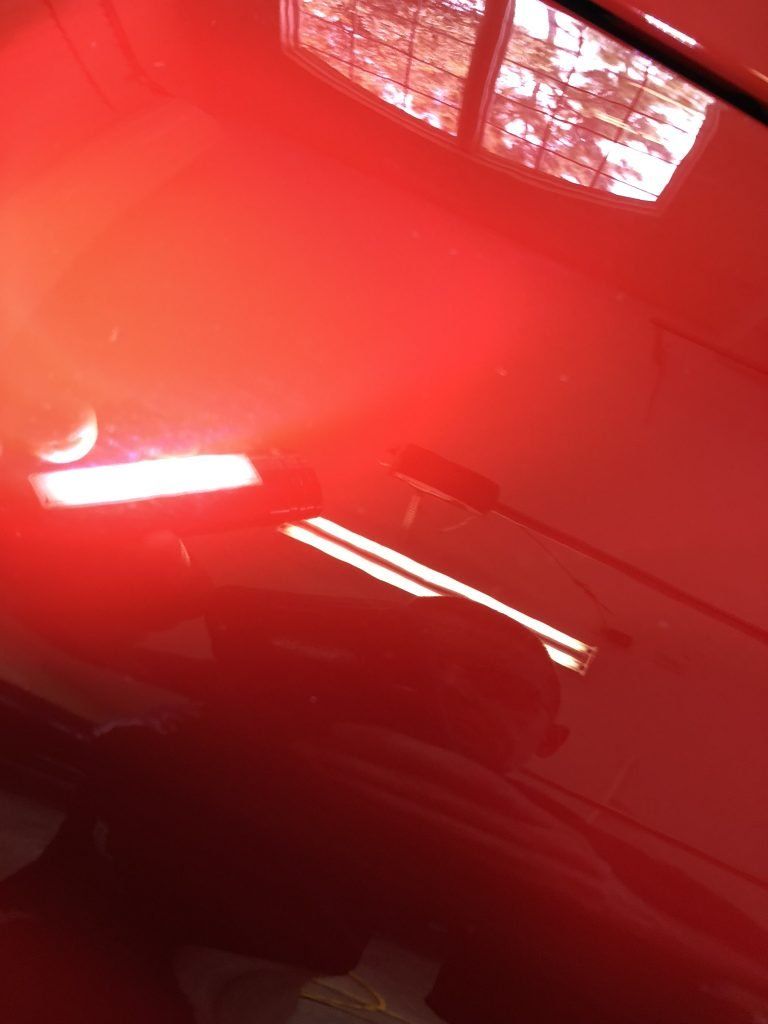 A red light is shining on a red car in a garage.