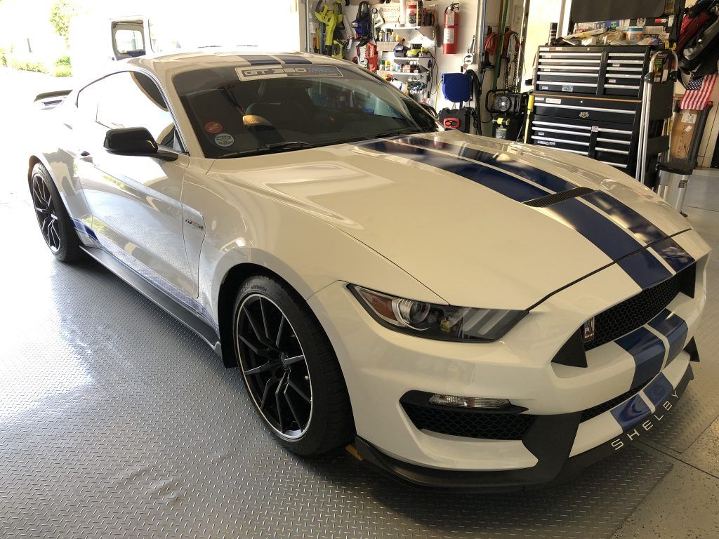 A white ford mustang with blue stripes is parked in a garage.