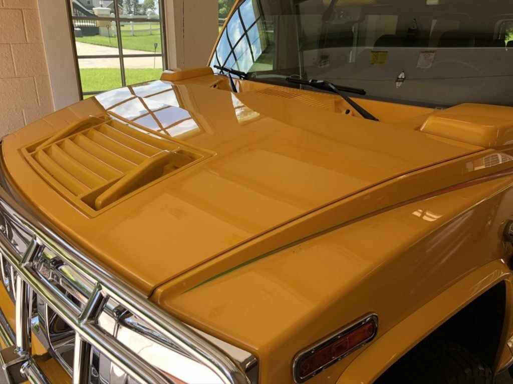 A yellow hummer is parked in a garage with the hood up.