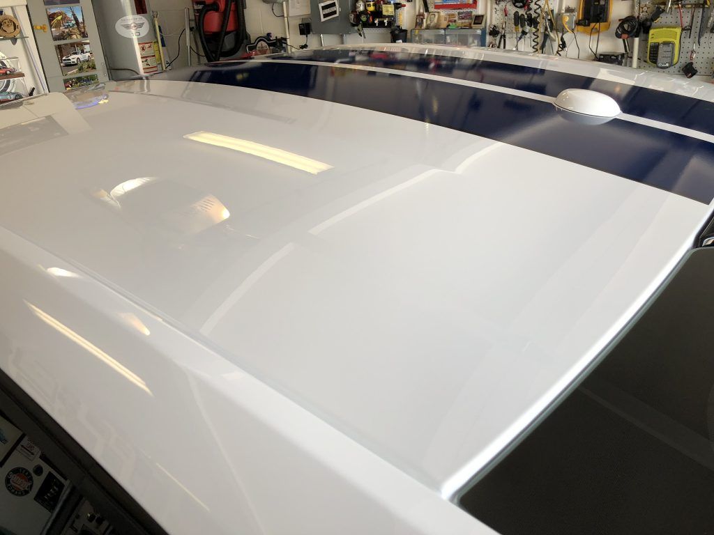 A white car with blue stripes on the roof is parked in a garage.
