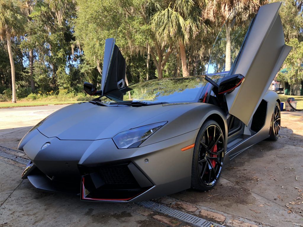 A gray lamborghini aventador with its doors open is parked on the side of the road.