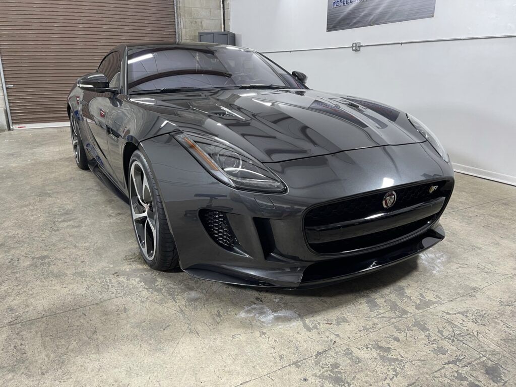 A black jaguar f type is parked in a garage.