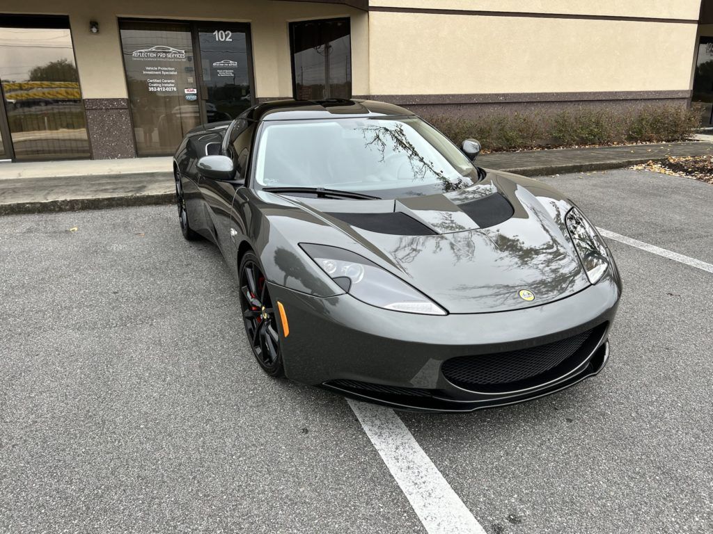 A gray sports car is parked in a parking lot in front of a building.