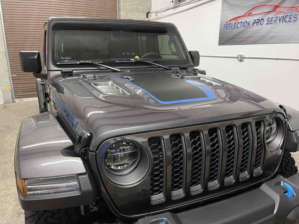 A gray jeep with a blue stripe on the hood is parked in a garage.