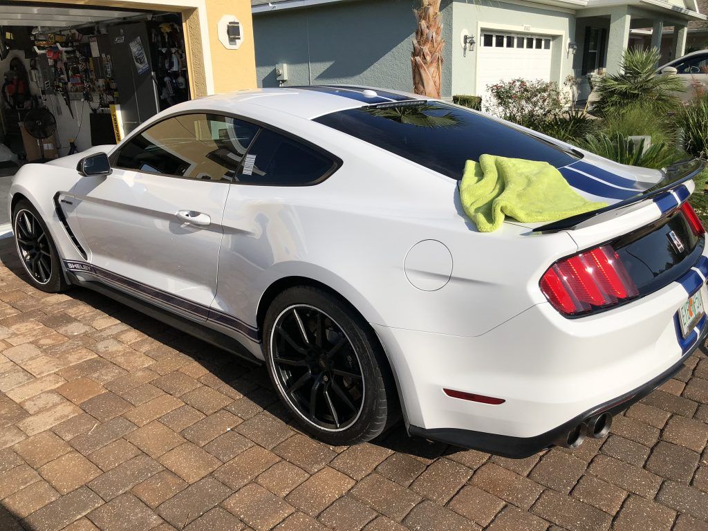 A white ford mustang is parked in front of a garage.