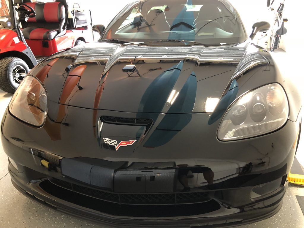 A black sports car is parked in a garage next to a golf cart.