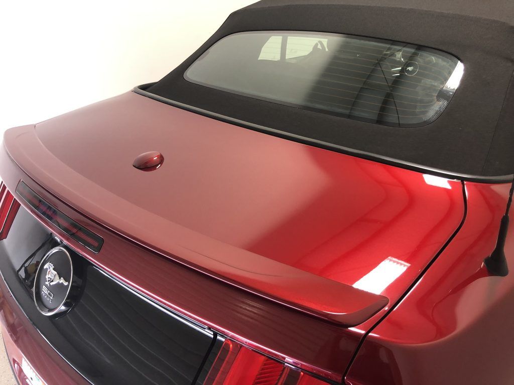 A red mustang with a black top is parked in a garage