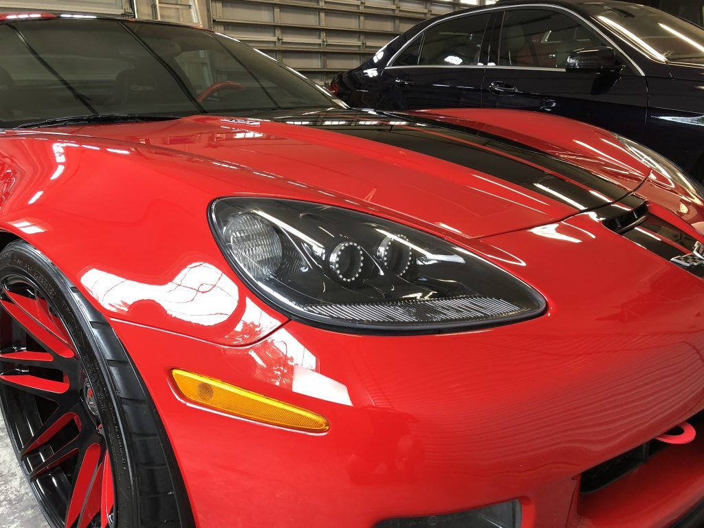 A red sports car is parked next to a black car in a garage.