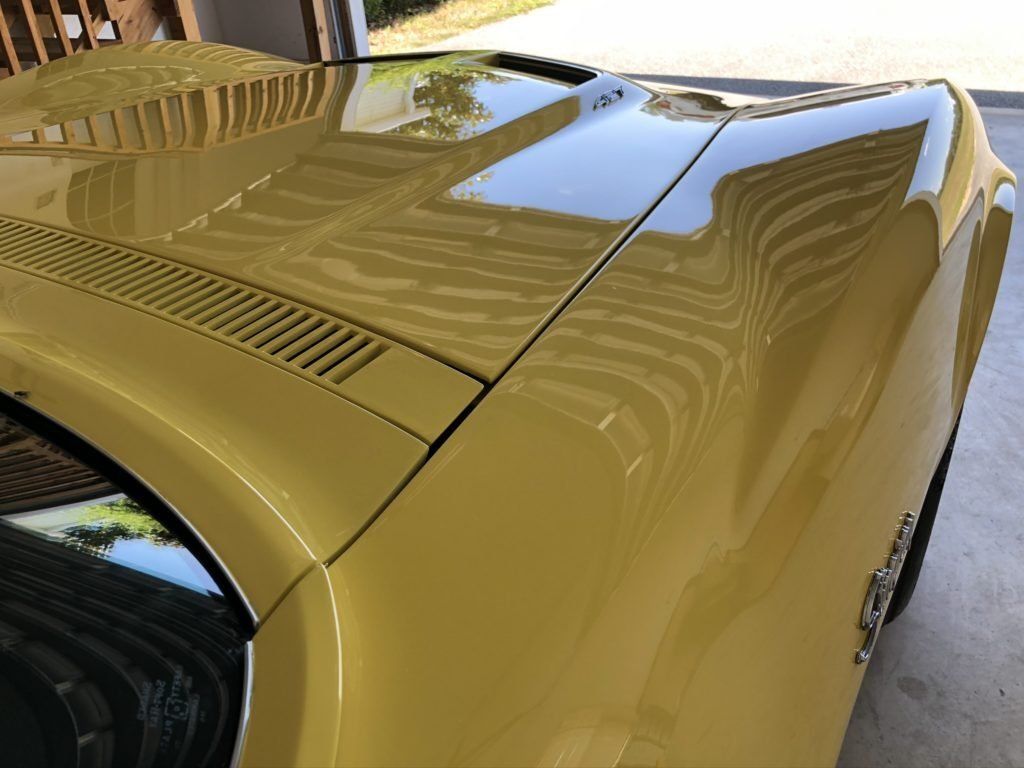 A yellow car is parked in a garage with the hood up.