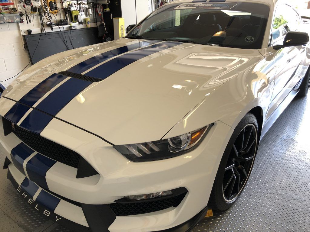 A white ford mustang with blue stripes is parked in a garage.