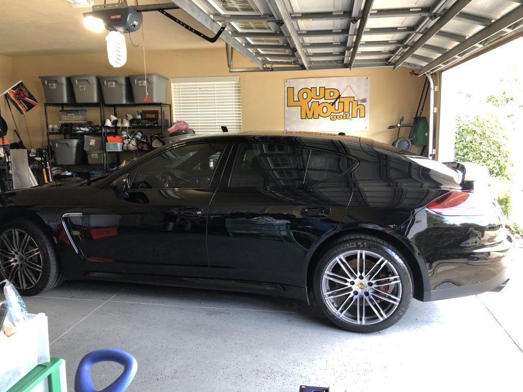 A black car is parked in a garage with a sign on the wall that says loud health.
