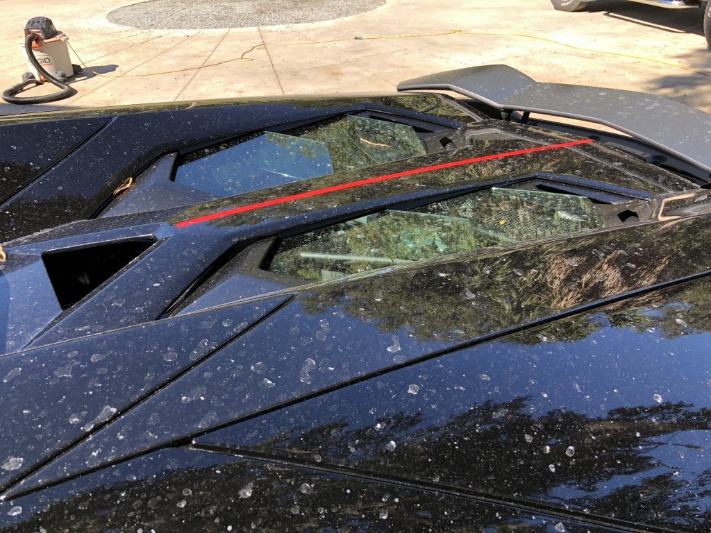 A black car with a broken windshield is parked in a parking lot.