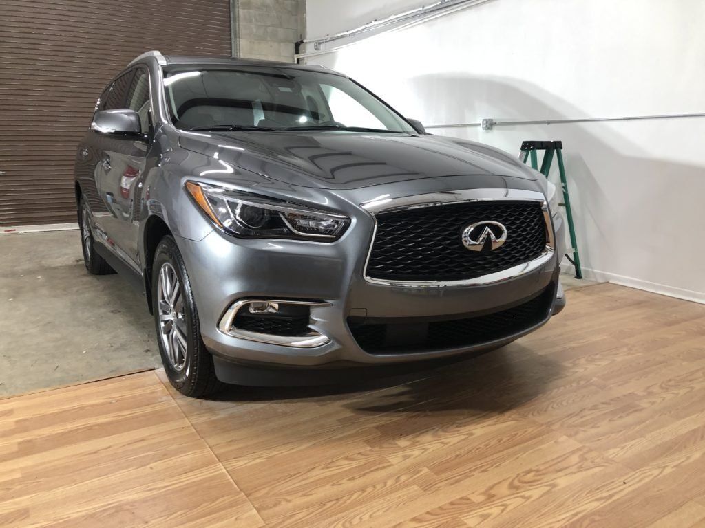 A silver infiniti q50 is parked in a garage next to a ladder.