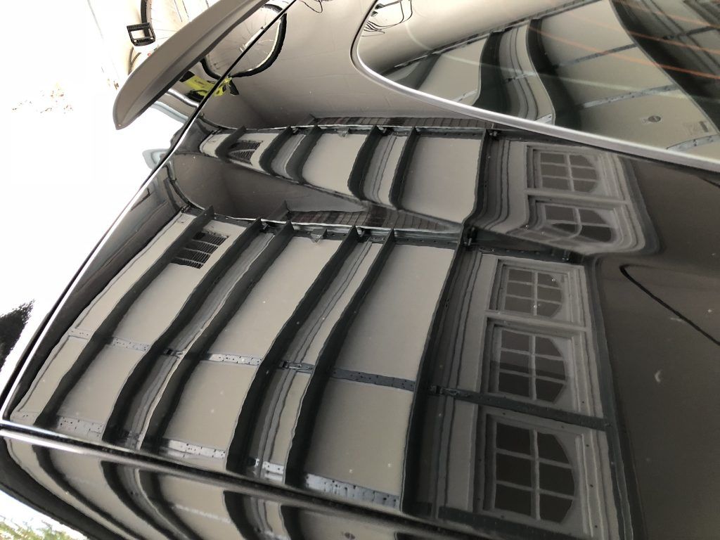 A close up of the hood of a car with a reflection of a building.