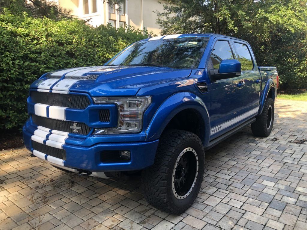 A blue ford f150 is parked on a brick driveway.