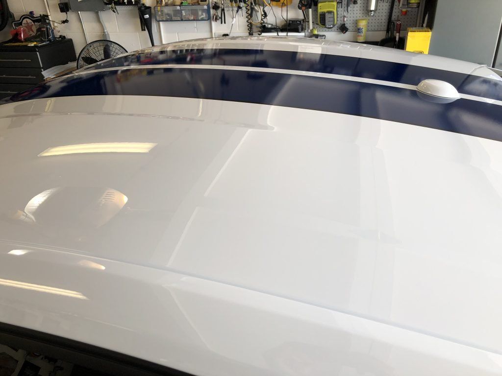 A white car with blue stripes on the hood is parked in a garage.