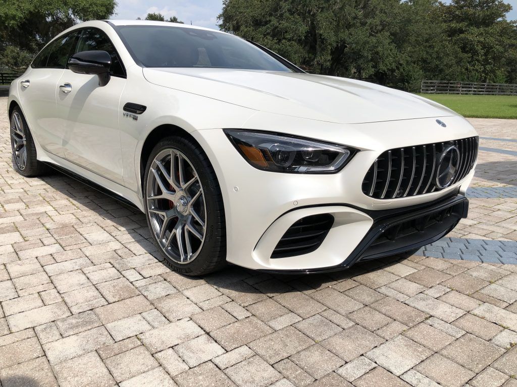 A white mercedes amg gt 63 s is parked on a brick driveway.