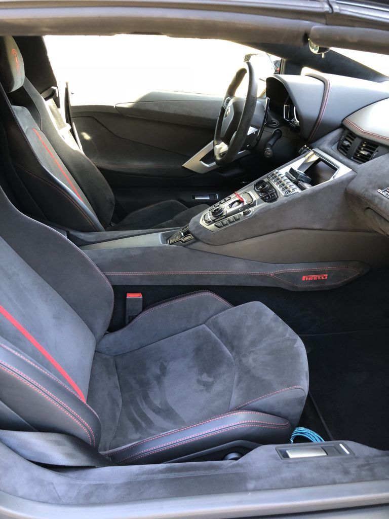 The interior of a lamborghini aventador with a red stripe on the seat.