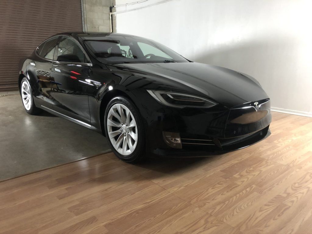A black tesla model s is parked on a wooden floor in a garage.