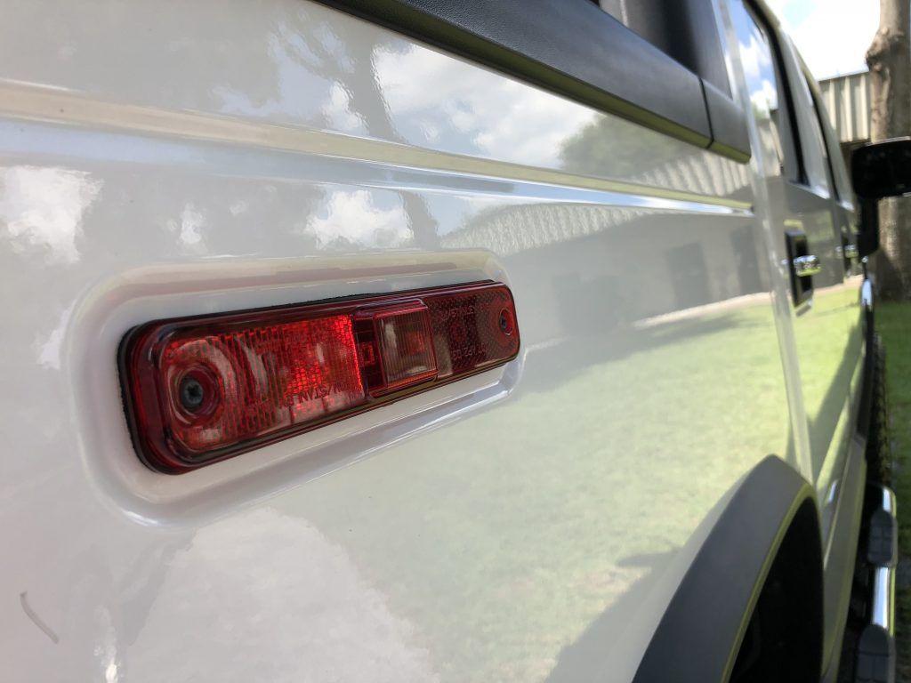 A white truck with a red tail light on the side of it.