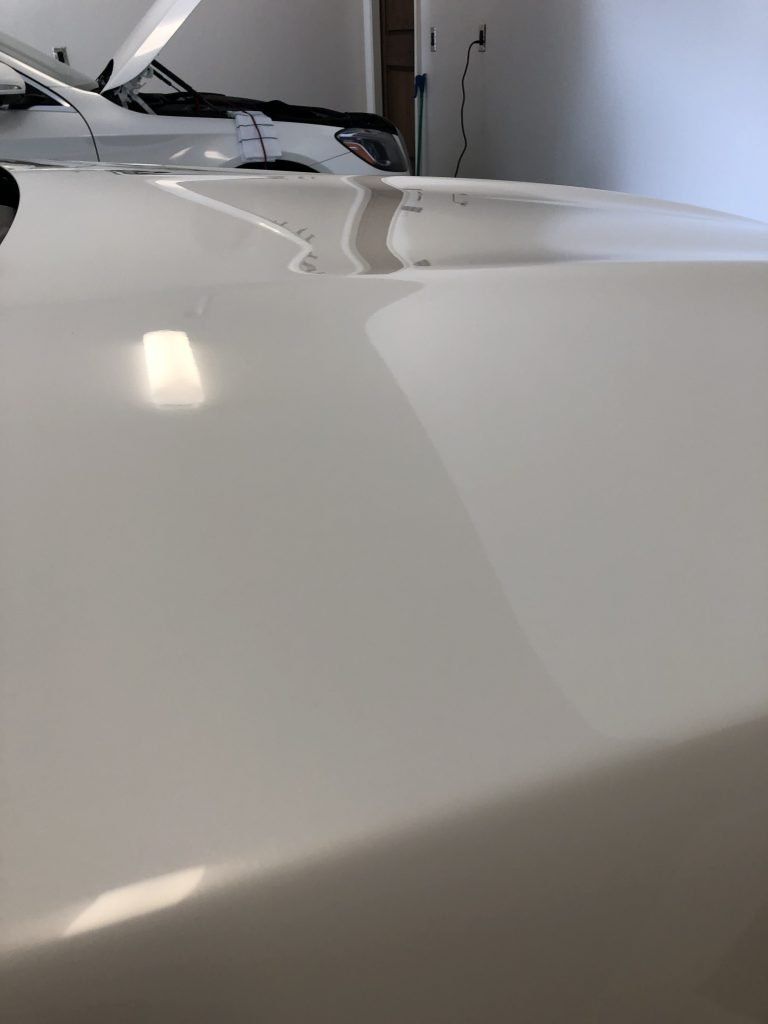 A white car is parked in a garage with the hood up.